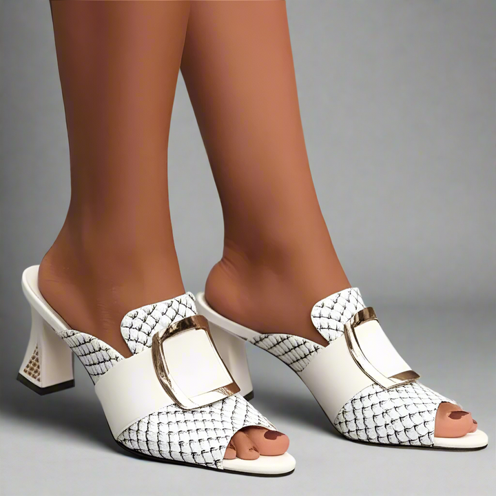 White high-heeled shoes with patterned straps worn by a person on a light background