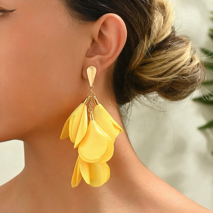 A person wearing yellow cascading petal-like earrings with a gold-tone teardrop post.
