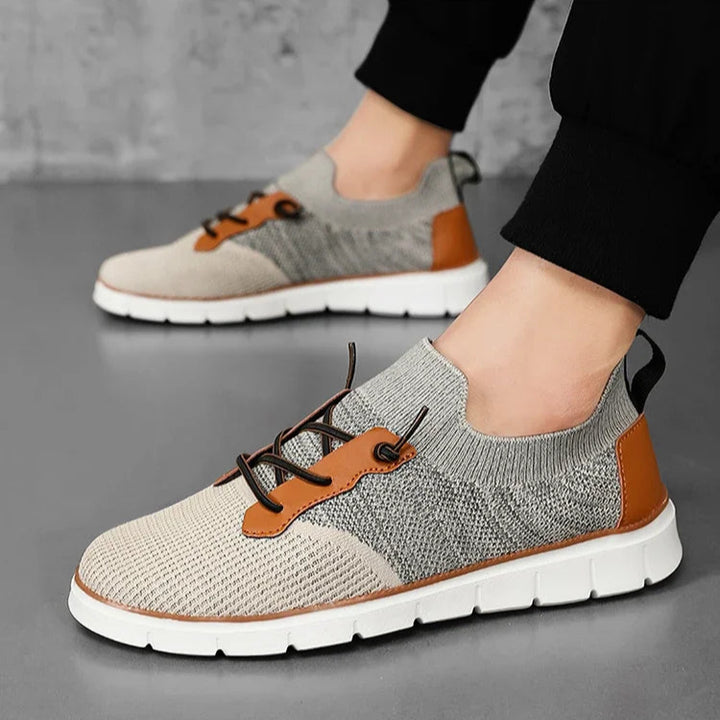 Gray and brown casual shoes worn by a person on a gray surface.