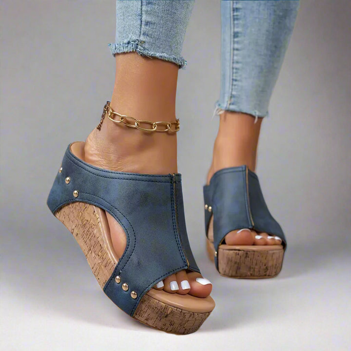 Blue wedge sandals with cork soles worn by a person, with a neutral background.