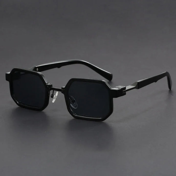 A pair of sunglasses with a unique octagonal frame, black with black lenses, displayed against a grey background.