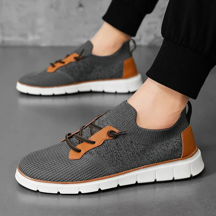 Gray sneakers with brown accents worn by a person on a gray background
