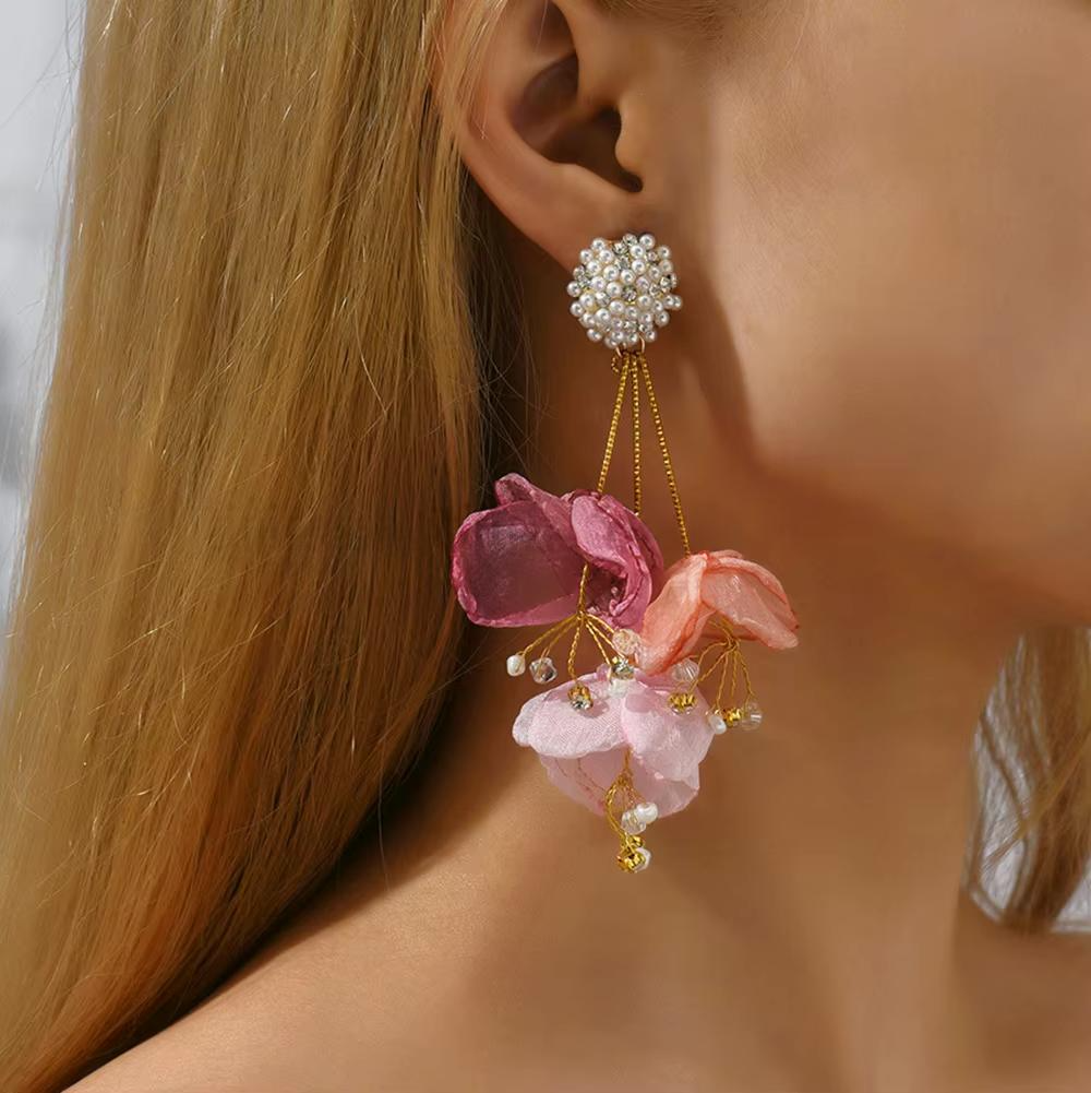 A person wearing a floral drop earring with translucent pink petals and a sparkling crystal stud.